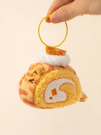 Plush keychain shaped like a roll cake with whipped cream and an orange slice on a beige background