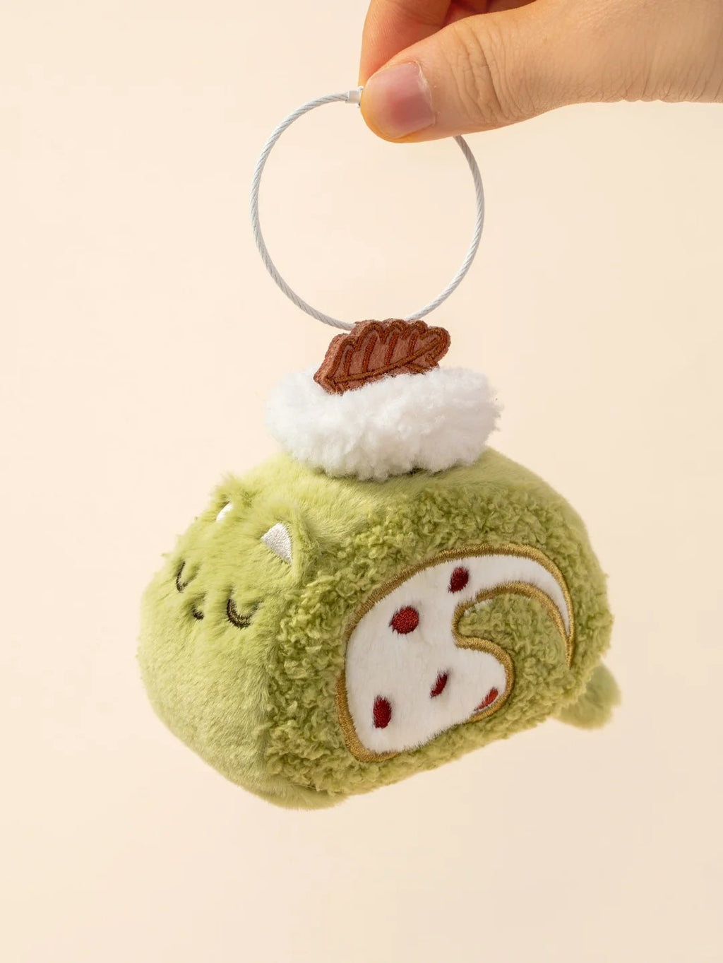 Plush keychain shaped like a green swiss roll with a brown cookie on a beige background