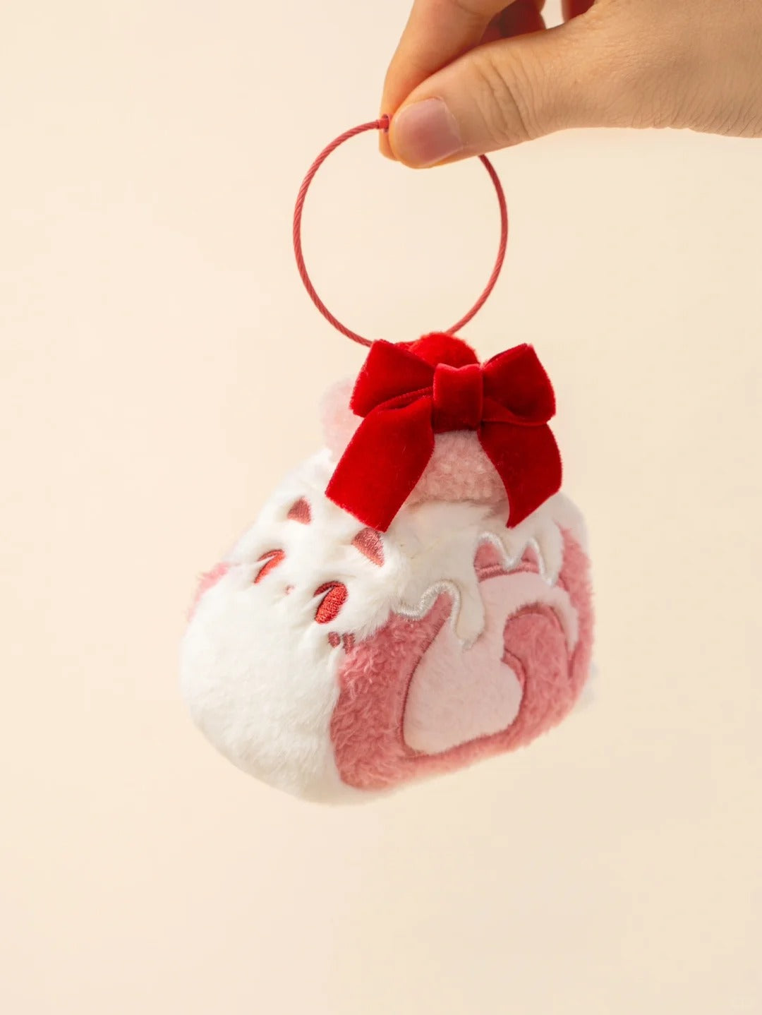 Small plush charm with a red bow held by a hand on a beige background