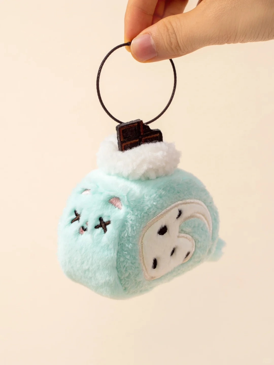 Plush keychain with cartoon face design held by a hand on a beige background