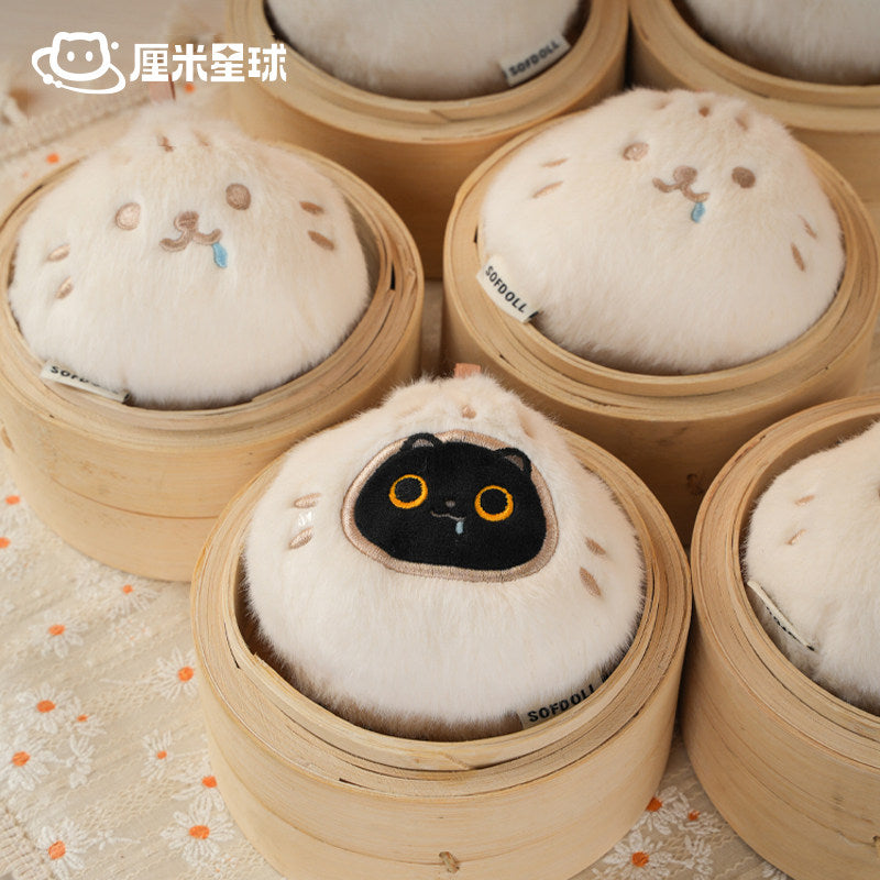 Plush toys shaped like buns with a black cat face design inside a bamboo steamer.