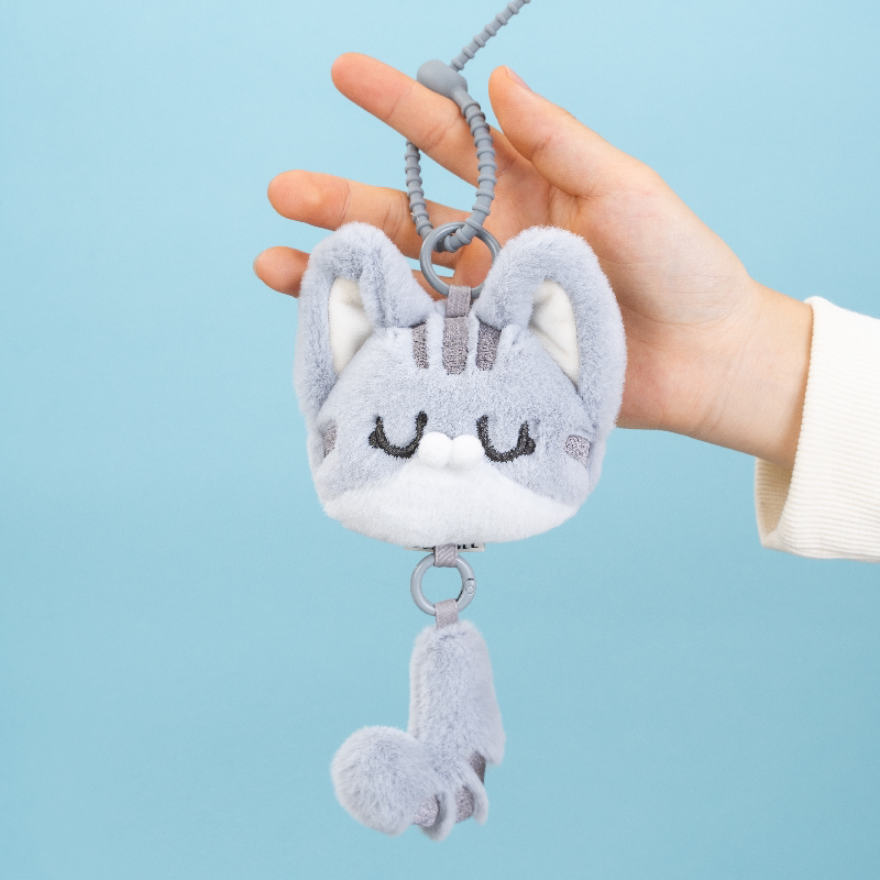 Plush keychain shaped like a cat held by a hand against a light blue background