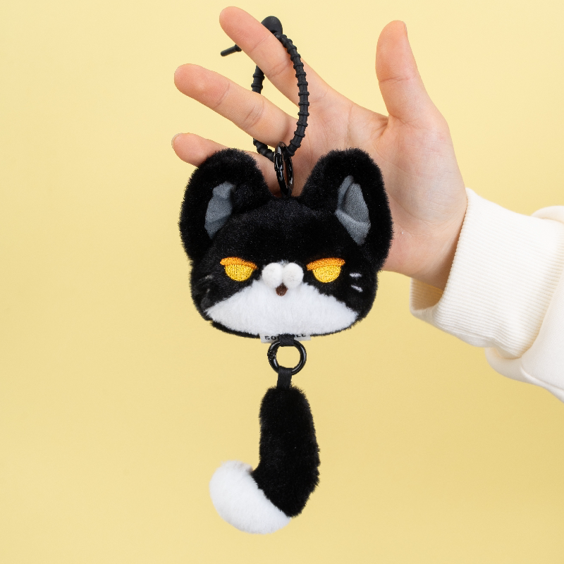 Hand holding a plush keychain shaped like a cat with a tail.