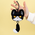 Hand holding a plush keychain shaped like a cat with a tail.