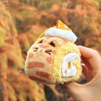 Plush toy resembling a cat as a Swiss roll held in front of autumn foliage.