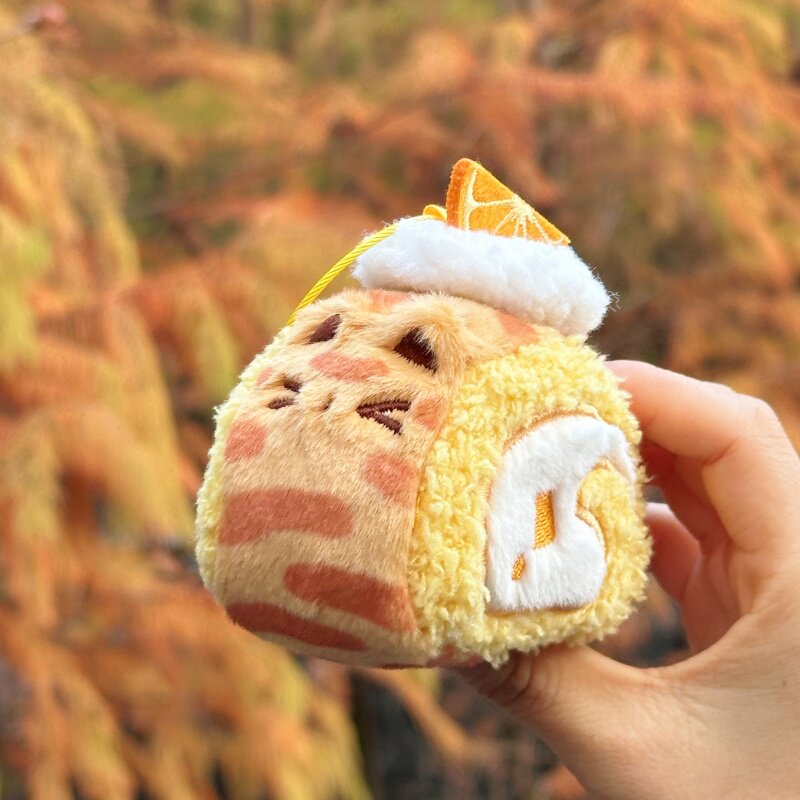 Plush toy resembling a cat as a Swiss roll held in front of autumn foliage.