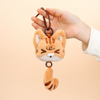 Plush cat keychain held by a hand against a beige background