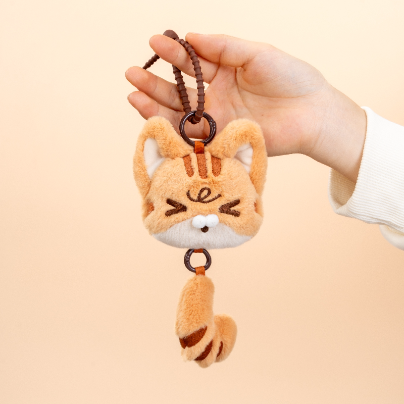 Plush cat keychain held by a hand against a beige background