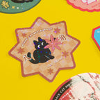 Star-shaped sticker with a black cat and star anise on a yellow background