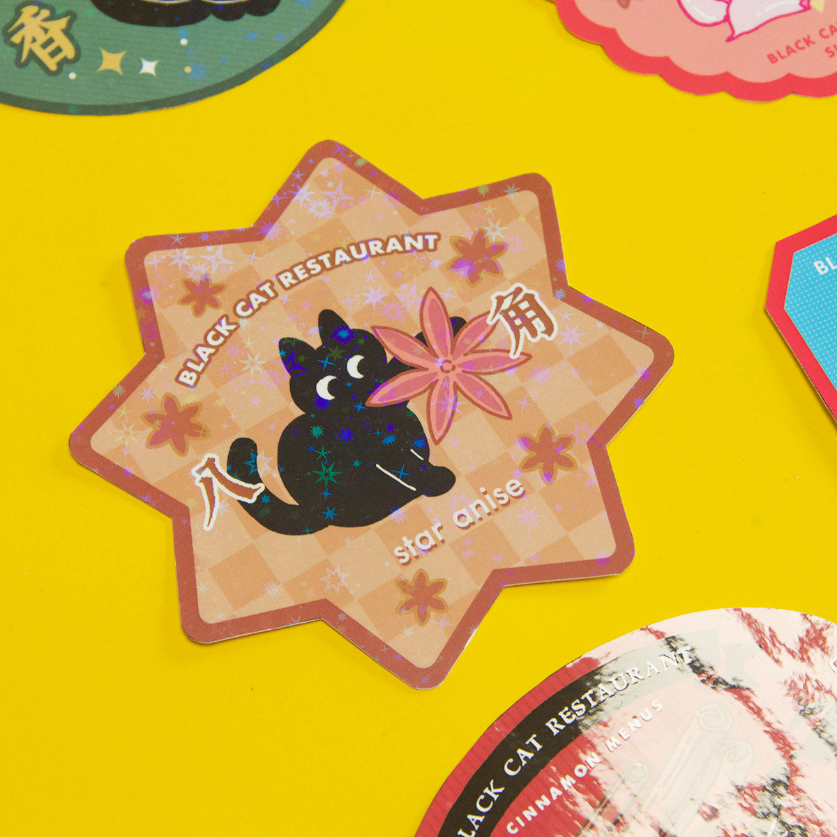 Star-shaped sticker with a black cat and star anise on a yellow background