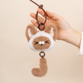 Hand holding a plush keychain shaped like a cat with a white chest on a beige background
