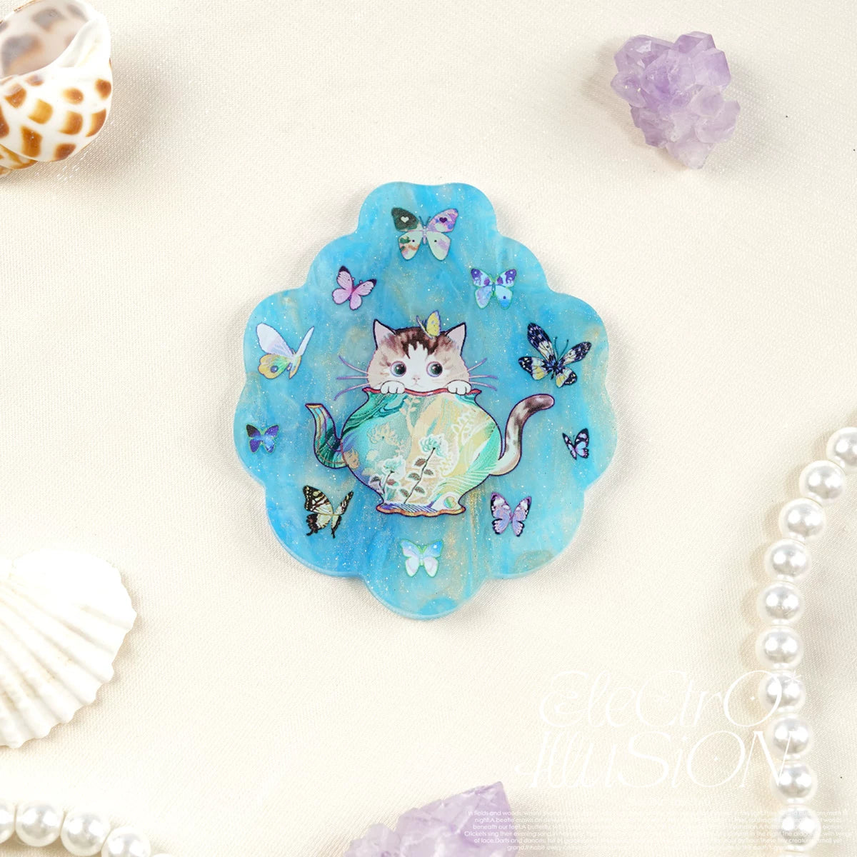Decorative magnet with a cat in a pot design on a blue scalloped mica acrylic, surrounded by butterflies and seashells.