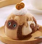 Plush toy resembling a cat as a dessert with a heart on top, sitting on a wooden plate.