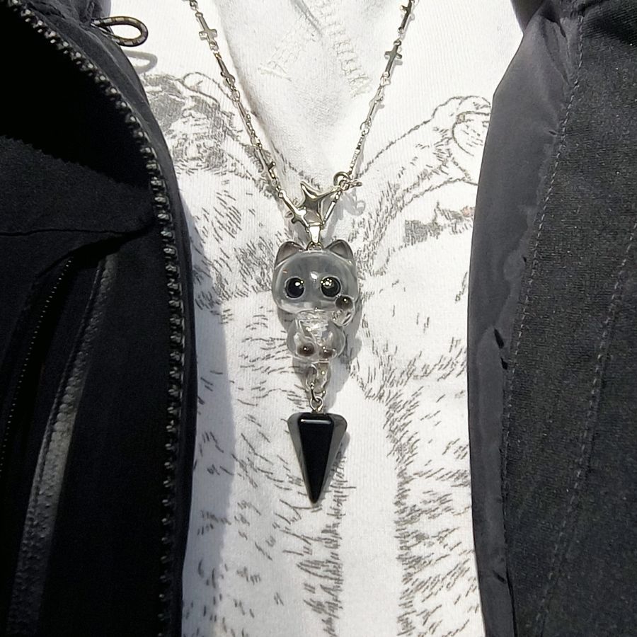 Necklace with a cat-shaped pendant and black triangle on a textured white background